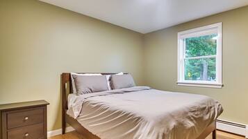 A bedroom with a bed, a nightstand, a window with a view of trees, and a ceiling light.