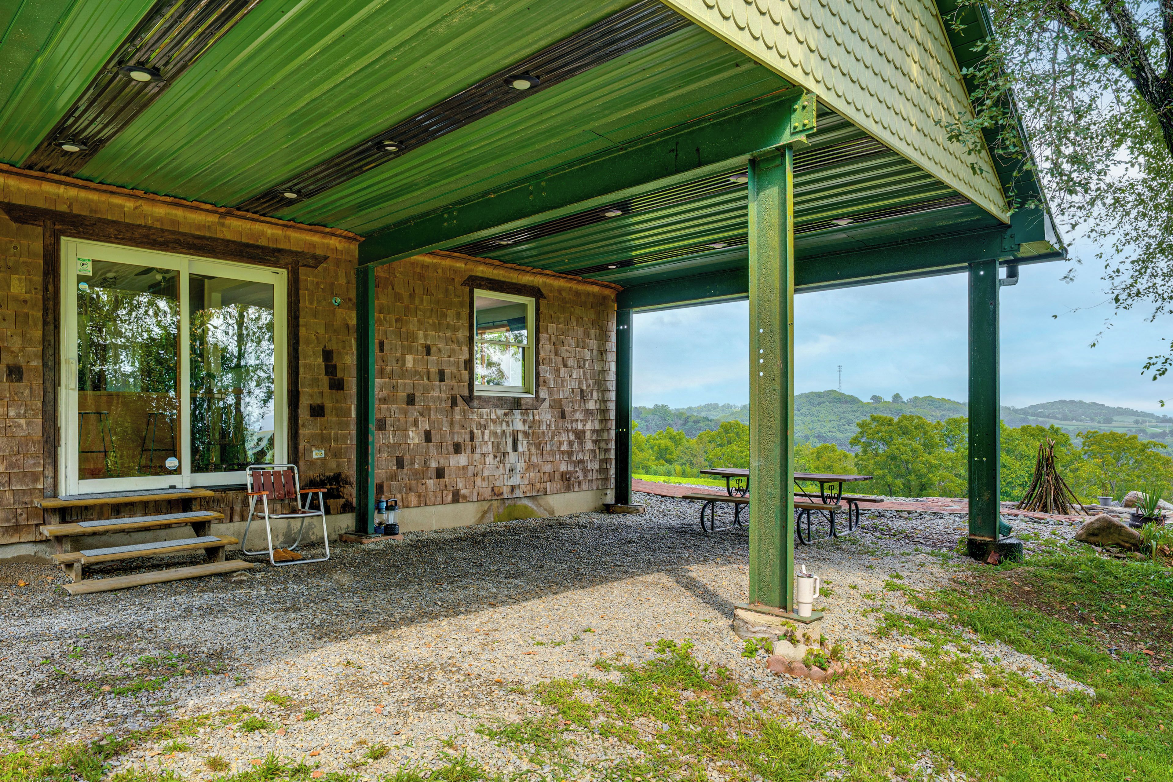 Um espaço ao ar livre coberto, com parede de pedra, um banco, uma mesa e vista para uma paisagem arborizada.