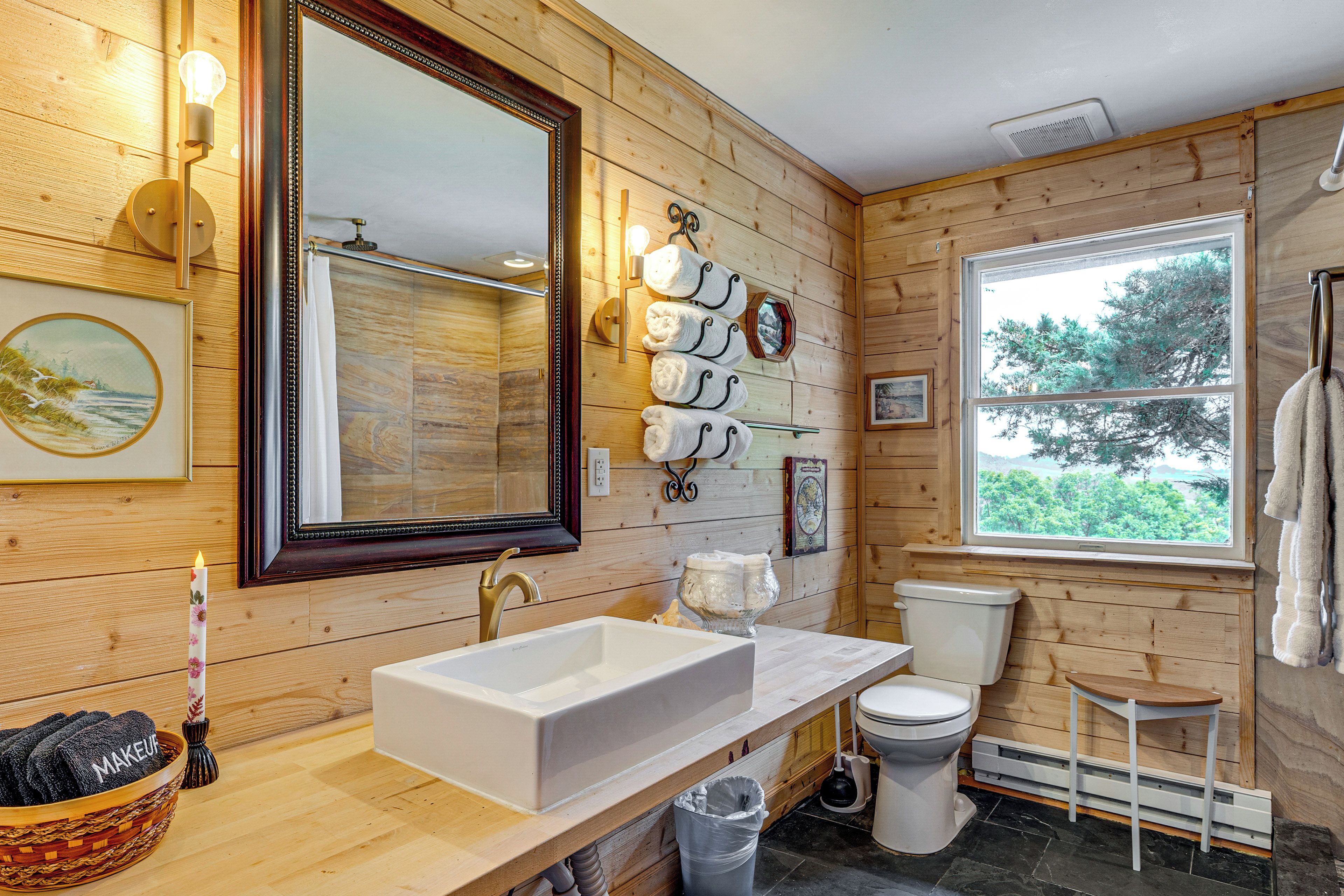 A wooden interior bathroom with a large mirror, a white sink, a toilet, and a window.
