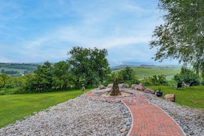 Un sendero pavimentado con un elemento central, rodeado de césped, árboles y una vista distante de colinas.