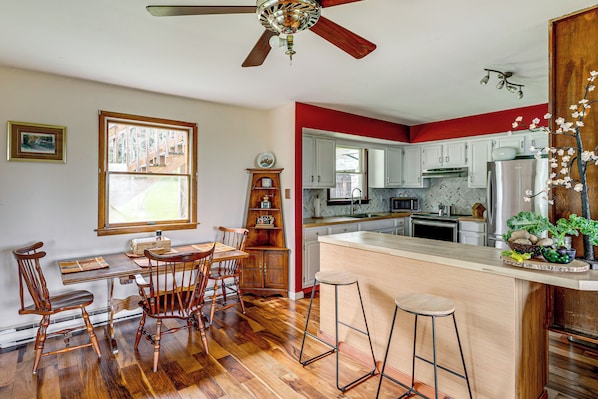 Una cocina con piso de madera, un comedor con mesa y sillas, y una barra con taburetes.