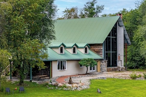 Una casa de dos pisos con techo verde, base de piedra y un ventanal grande a la derecha.