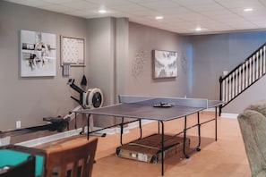 A ping pong table in a room with a treadmill, exercise equipment, and artwork on the walls.