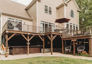 A two-story house with a covered patio area featuring a swing set, a wooden deck, and a sign that reads 'LAKE'.
