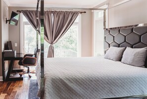 Quarto de hotel com uma cama, uma mesa de trabalho com cadeira, televisão de tela plana e janela com cortinas.