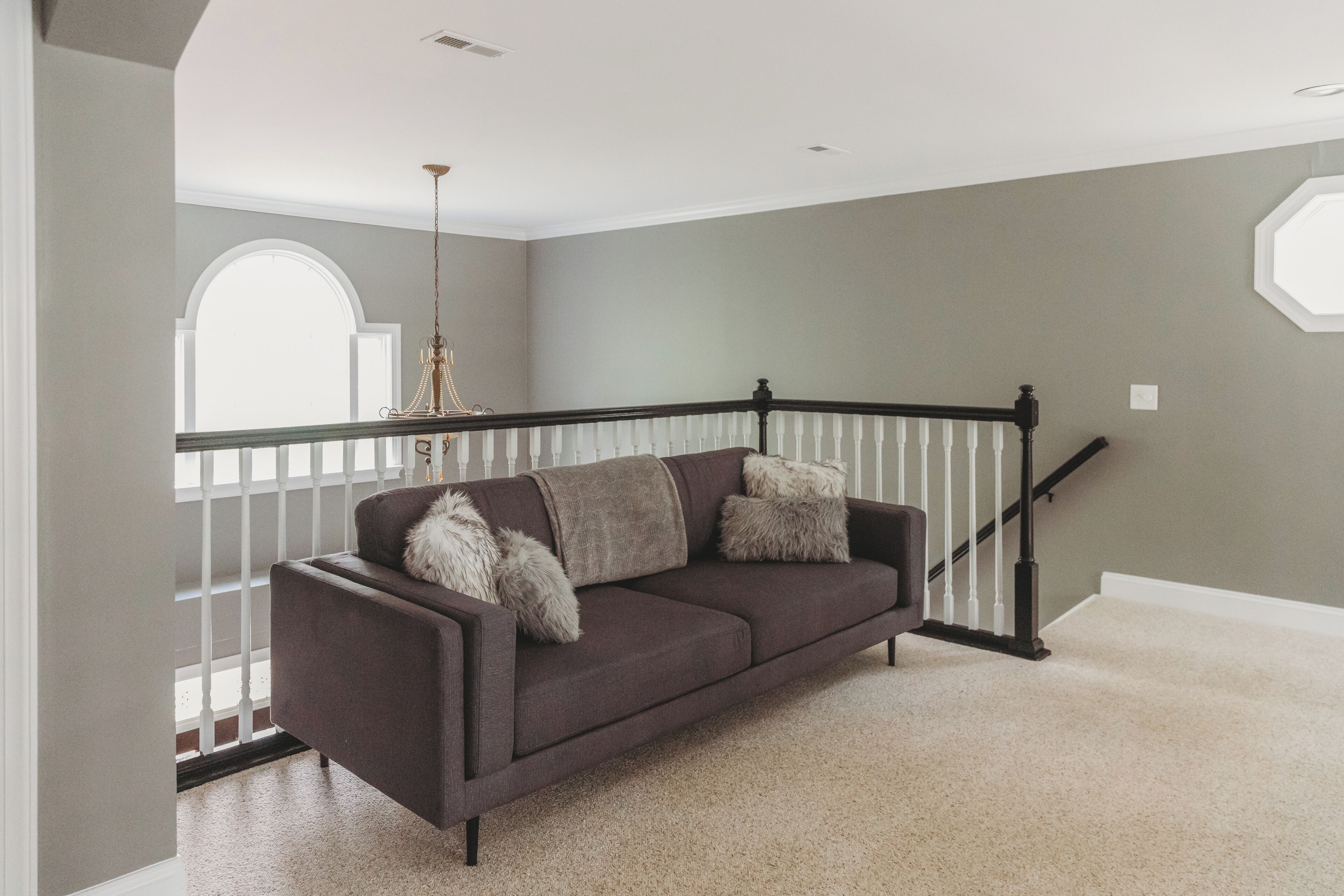 A living room with a dark brown sofa, white-framed windows, and a staircase.