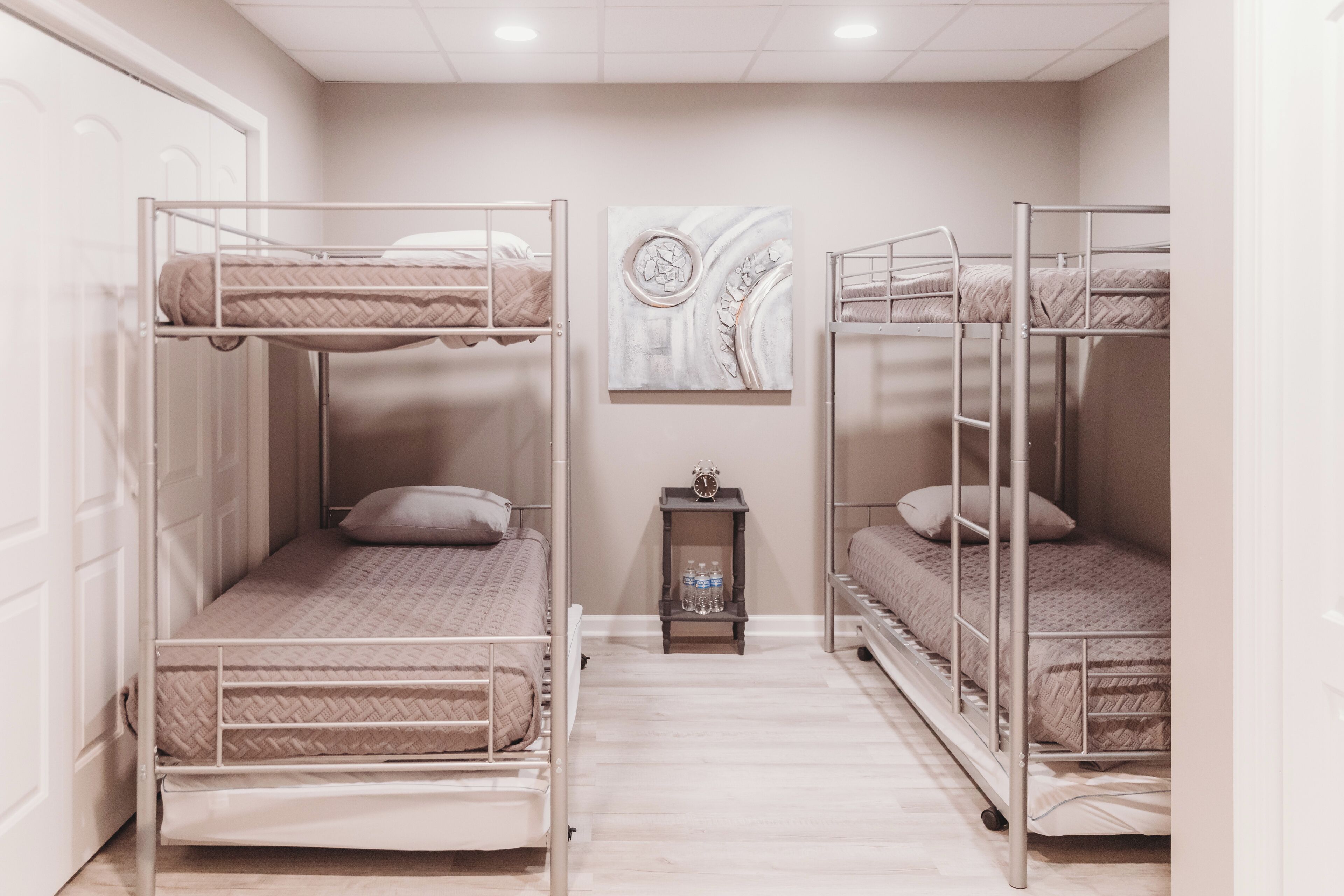 A room with bunk beds, a small table with bottles, and a painting on the wall.