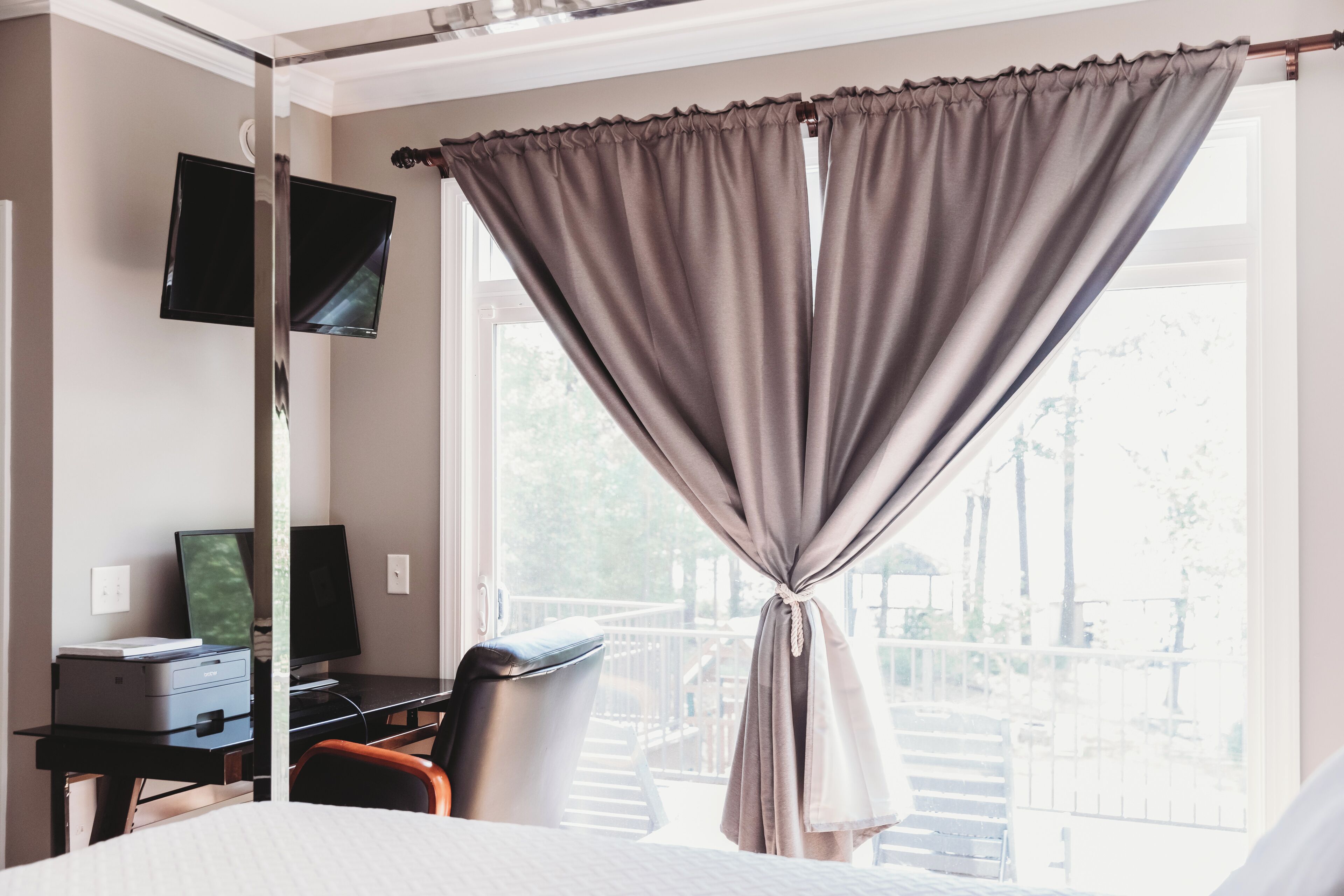 A hotel room with a bed, a desk with a computer, a chair, and a TV mounted on the wall.