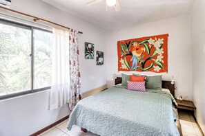 A bedroom with a bed, a window with curtains, a ceiling fan, and wall art. - Pool, Walk to Beach: Playas del Coco Studio (Sardinal)