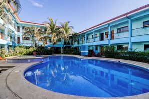A swimming pool surrounded by a multi-story building with balconies, palm trees, and a clear sky. - Pool, Walk to Beach: Playas del Coco Studio (Sardinal)