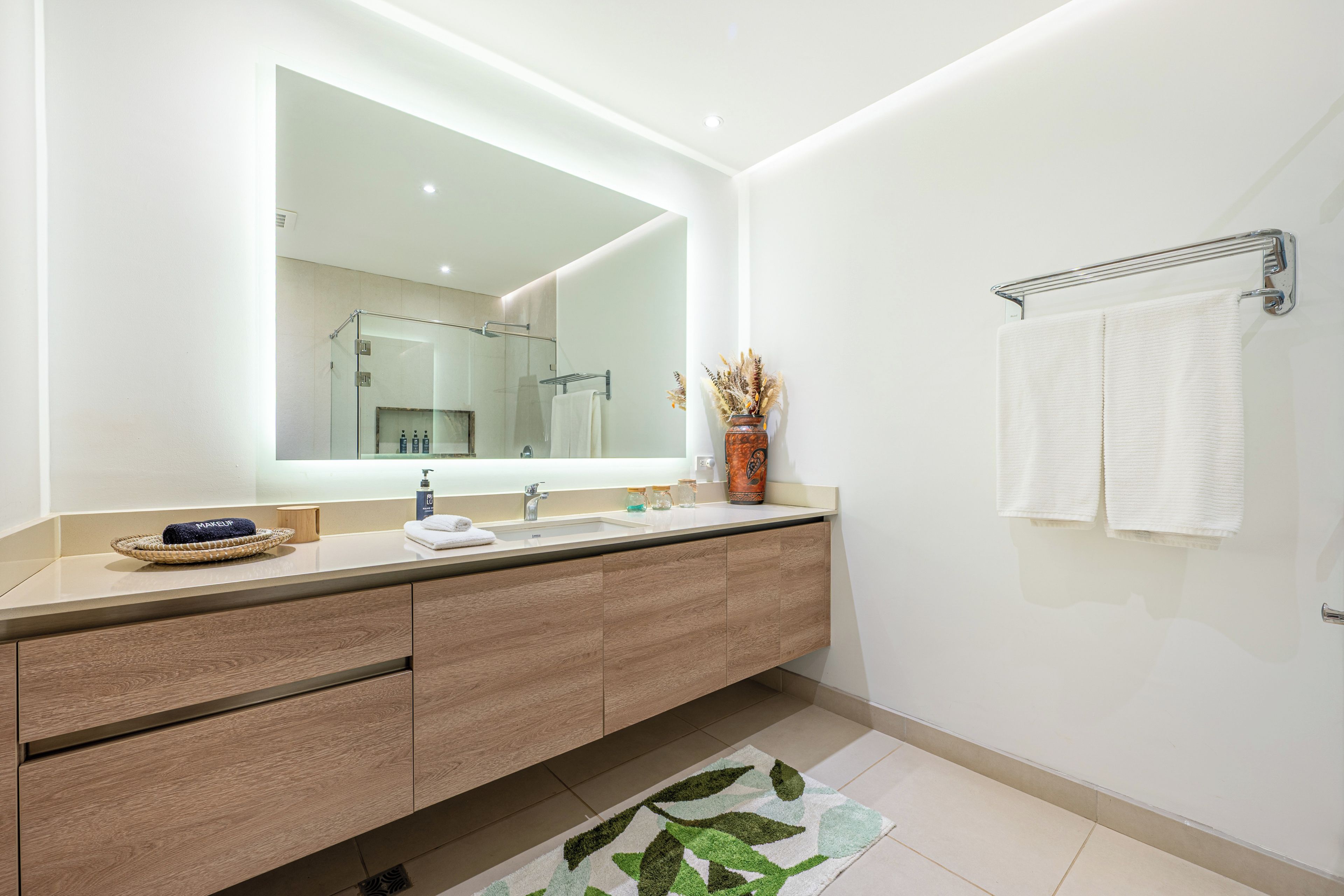 A modern bathroom with a large mirror, a wooden vanity, a towel rack, and a decorative vase.
