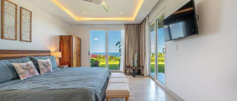Ein Schlafzimmer mit Bett, einer Bank, einem Deckenventilator, einem Fernseher und Blick ins Freie.