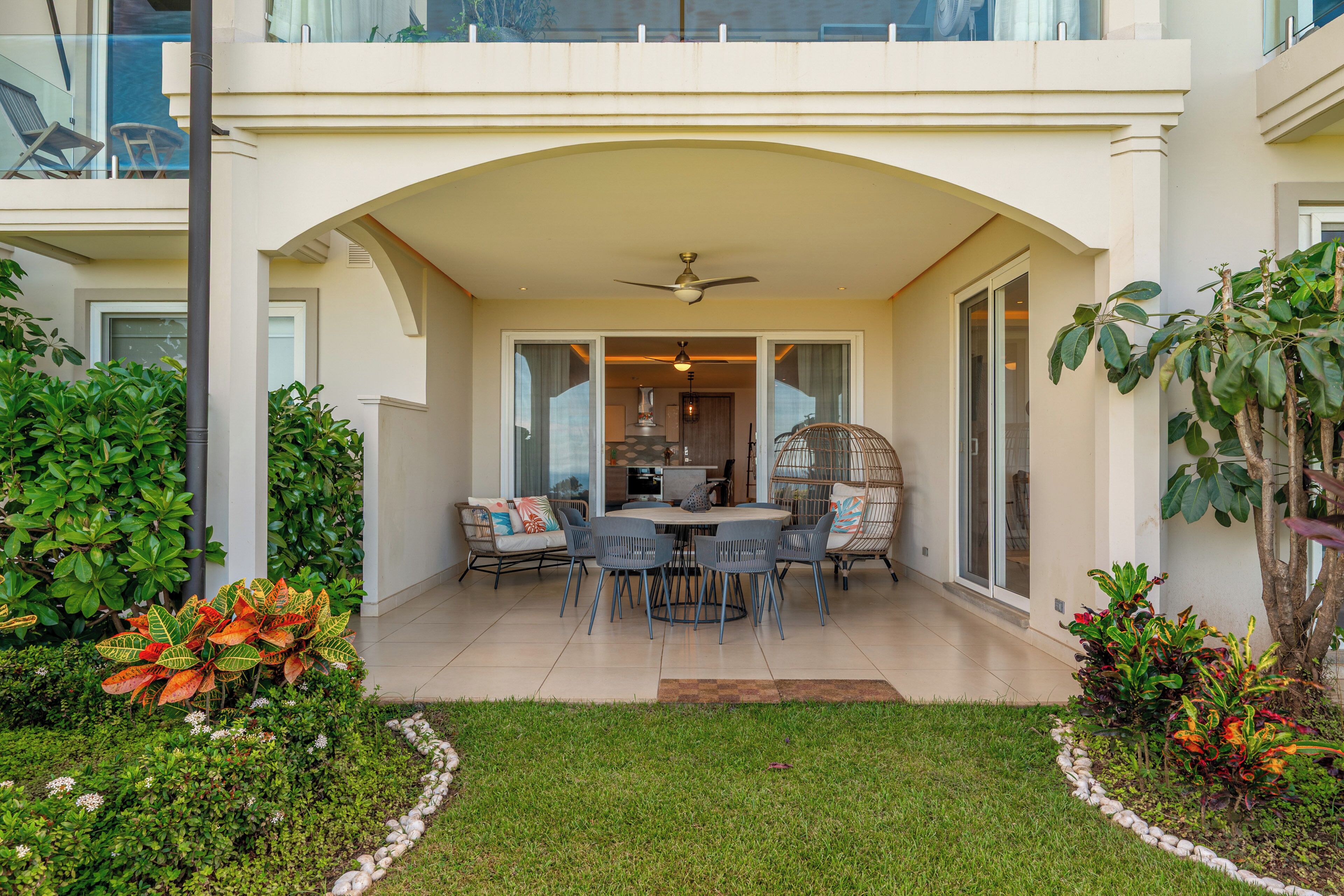 A covered patio area with a dining table and chairs, surrounded by greenery and a small garden.