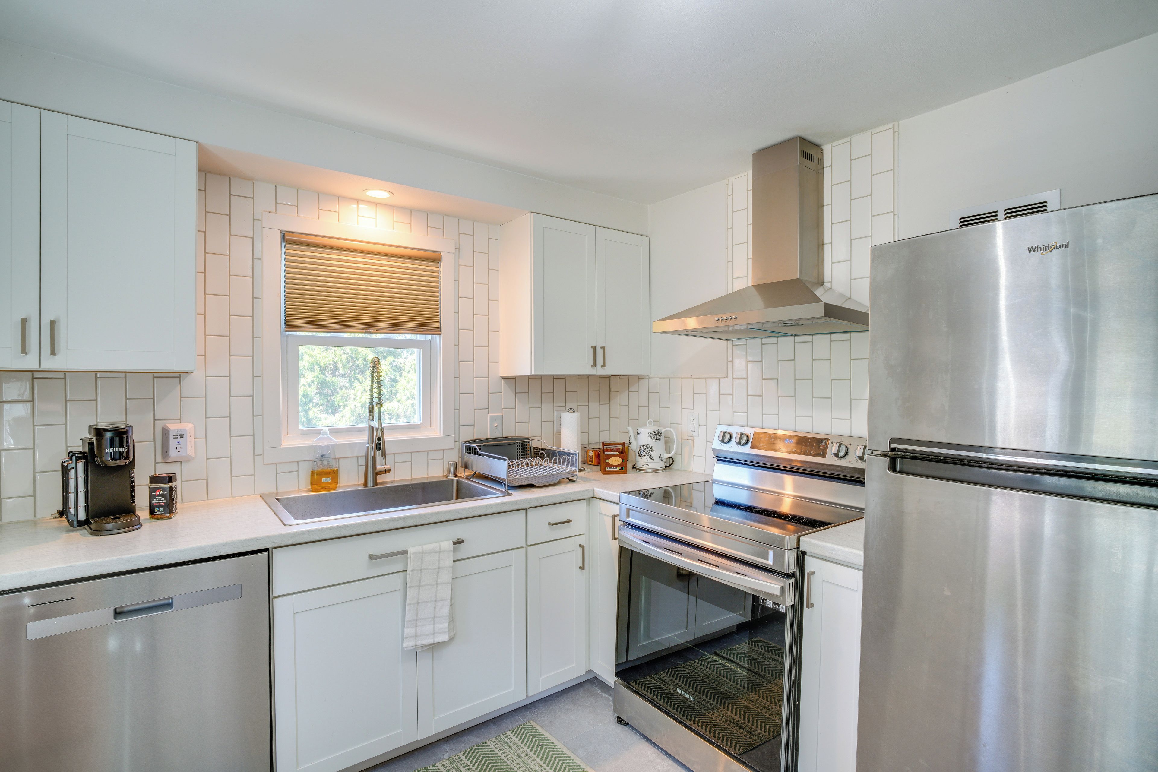A modern kitchen with white cabinetry, stainless steel appliances, and a window with blinds.