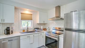 A modern kitchen with white cabinetry, stainless steel appliances, and a window with blinds.