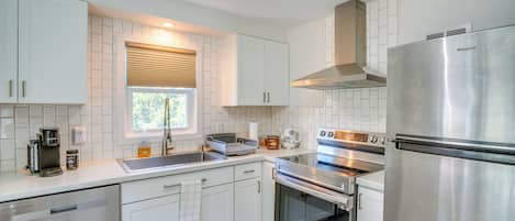 A modern kitchen with white cabinetry, stainless steel appliances, and a window with blinds.