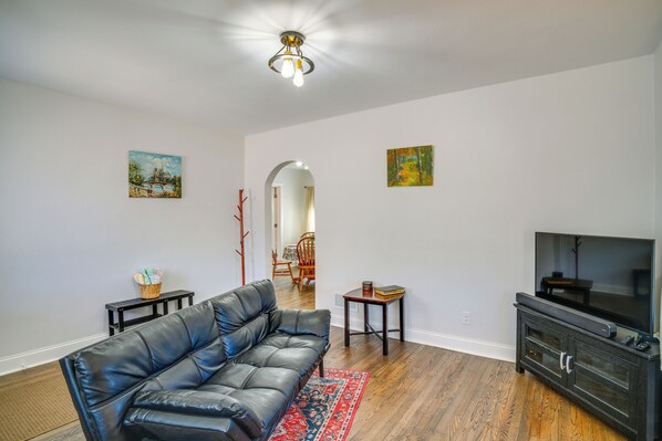 A living room with a black leather sofa, a television, a small table with a book, and two paintings on the wall.