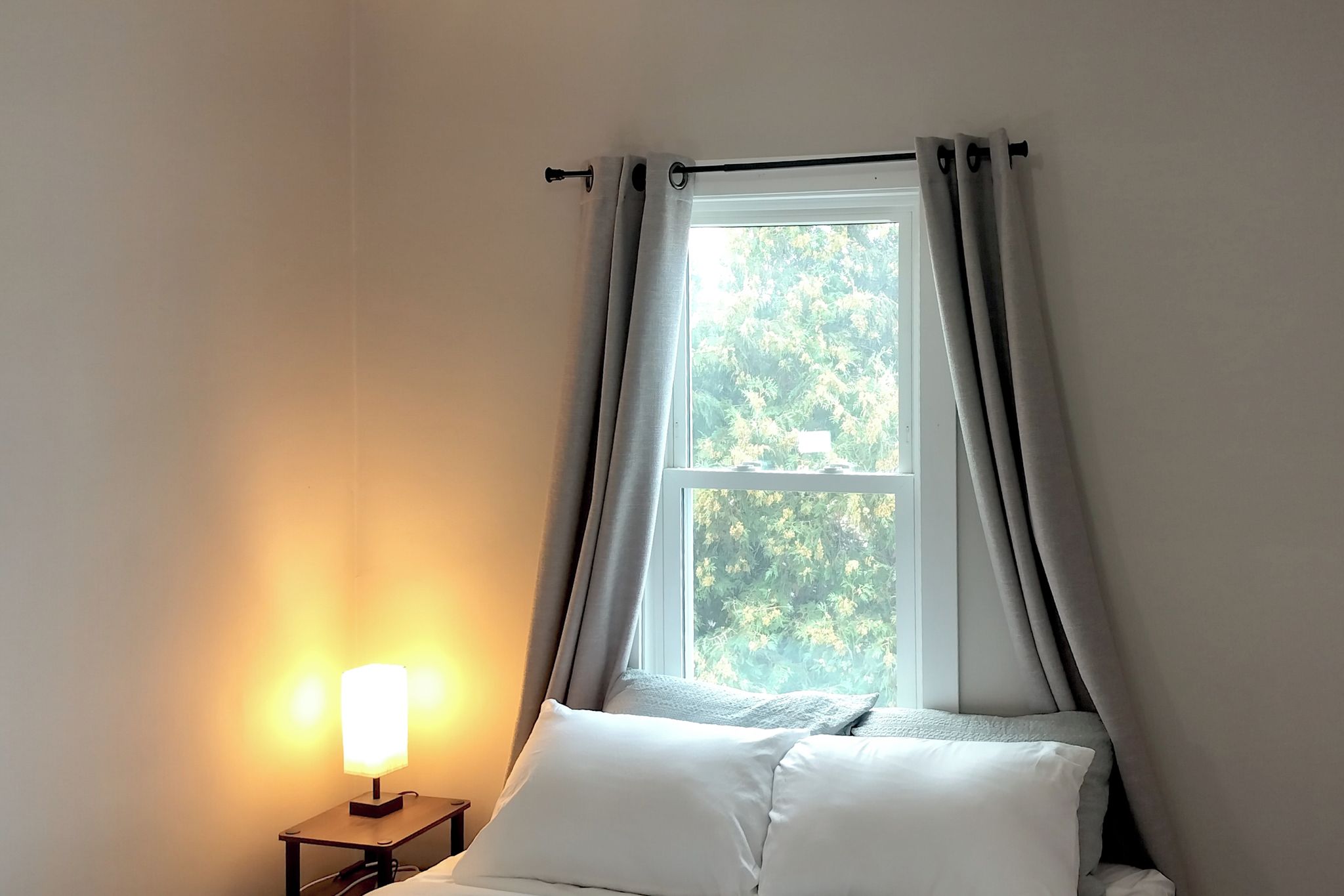 Een slaapkamer met een bed, een nachtkastje met een lamp en een raam met gordijnen.