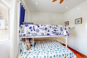 Ein Etagenbett mit blau-weiß gestreuter Bettwäsche im Seestil, ein Fenster mit Vorhängen und eine Wand mit Sternfisch-Verzierungen.