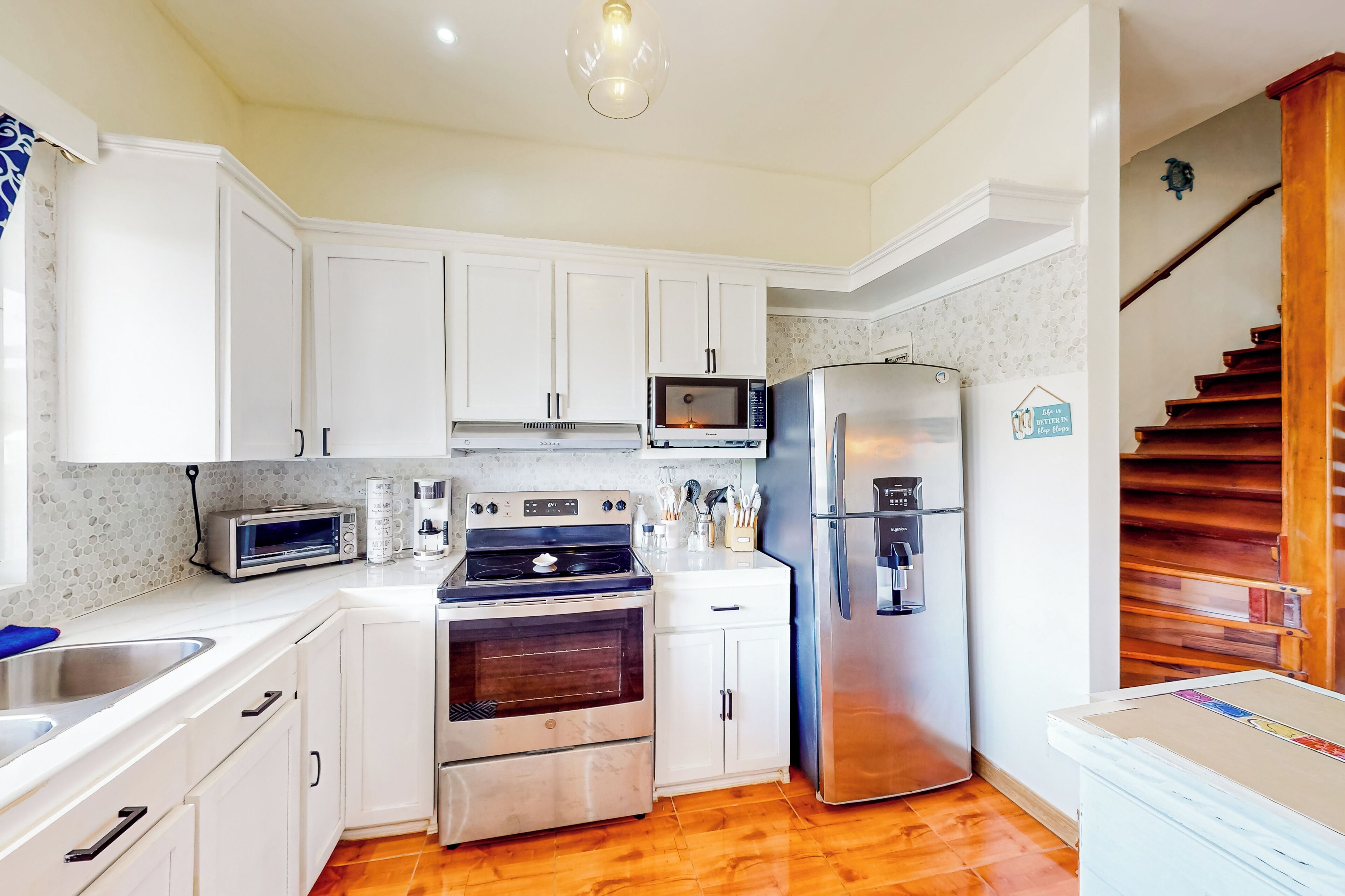 A compact kitchen with white cabinets, a stainless steel refrigerator, a microwave, a stove, and a toaster.