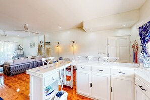 Ein gut beleuchteter Raum mit einem weißen Deckenventilator, einem Essbereich mit einem weißen Tisch und Stühlen sowie einem weißen Schrank mit Schubladen.