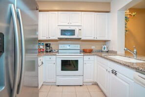 A kitchen with white cabinets, a microwave, an oven, a sink, and a stainless steel refrigerator.