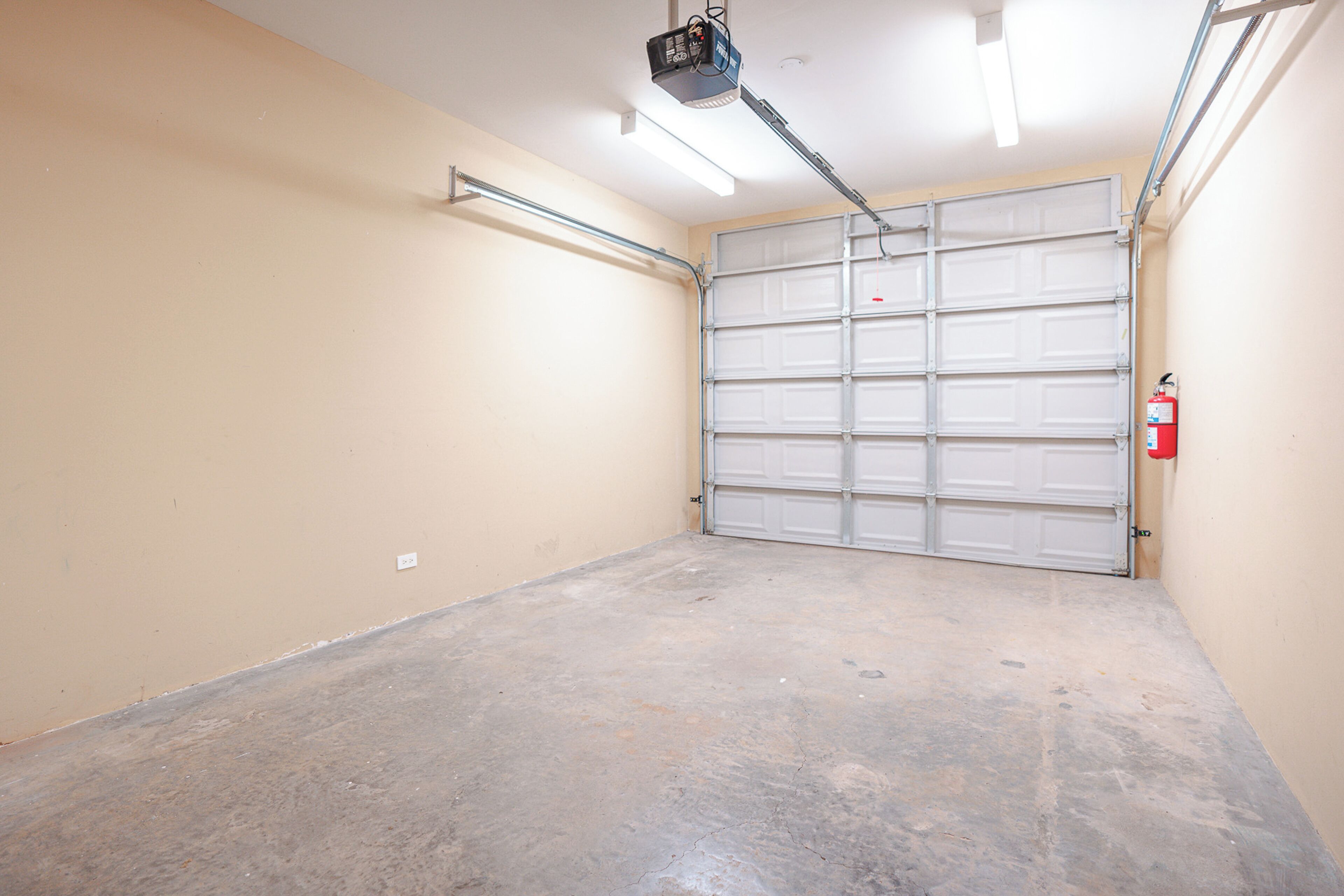 Un garaje con puerta cerrada, proyector en el techo y extintor en la pared.