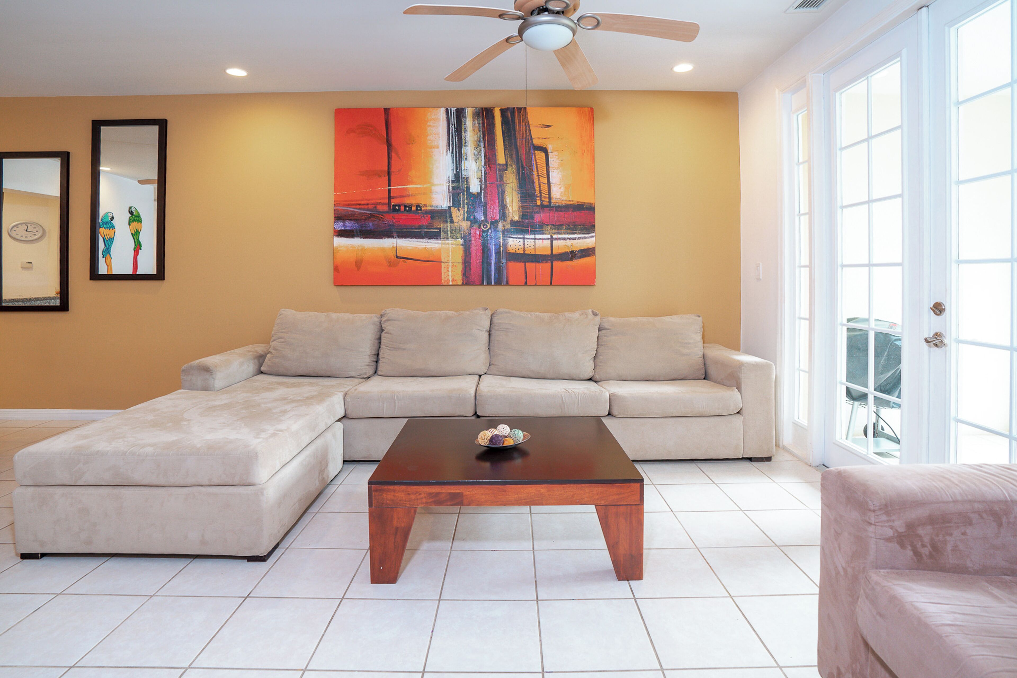 A living room with a sectional sofa, a coffee table, a ceiling fan, and a large abstract painting on the wall.