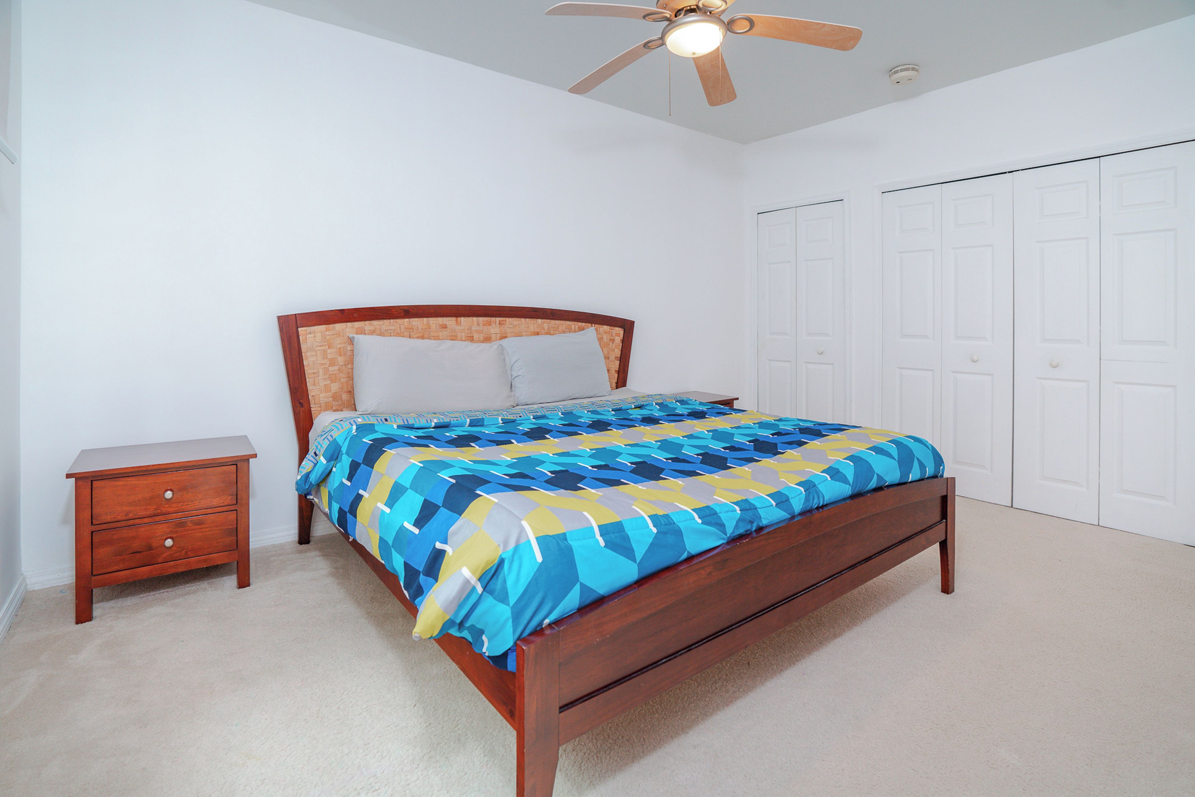 Quarto com cama de madeira, mesa de cabeceira, ventilador de teto e porta branca.
