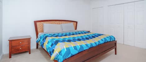Un dormitorio con cama de madera, una mesita de noche, un ventilador de techo y una puerta blanca.
