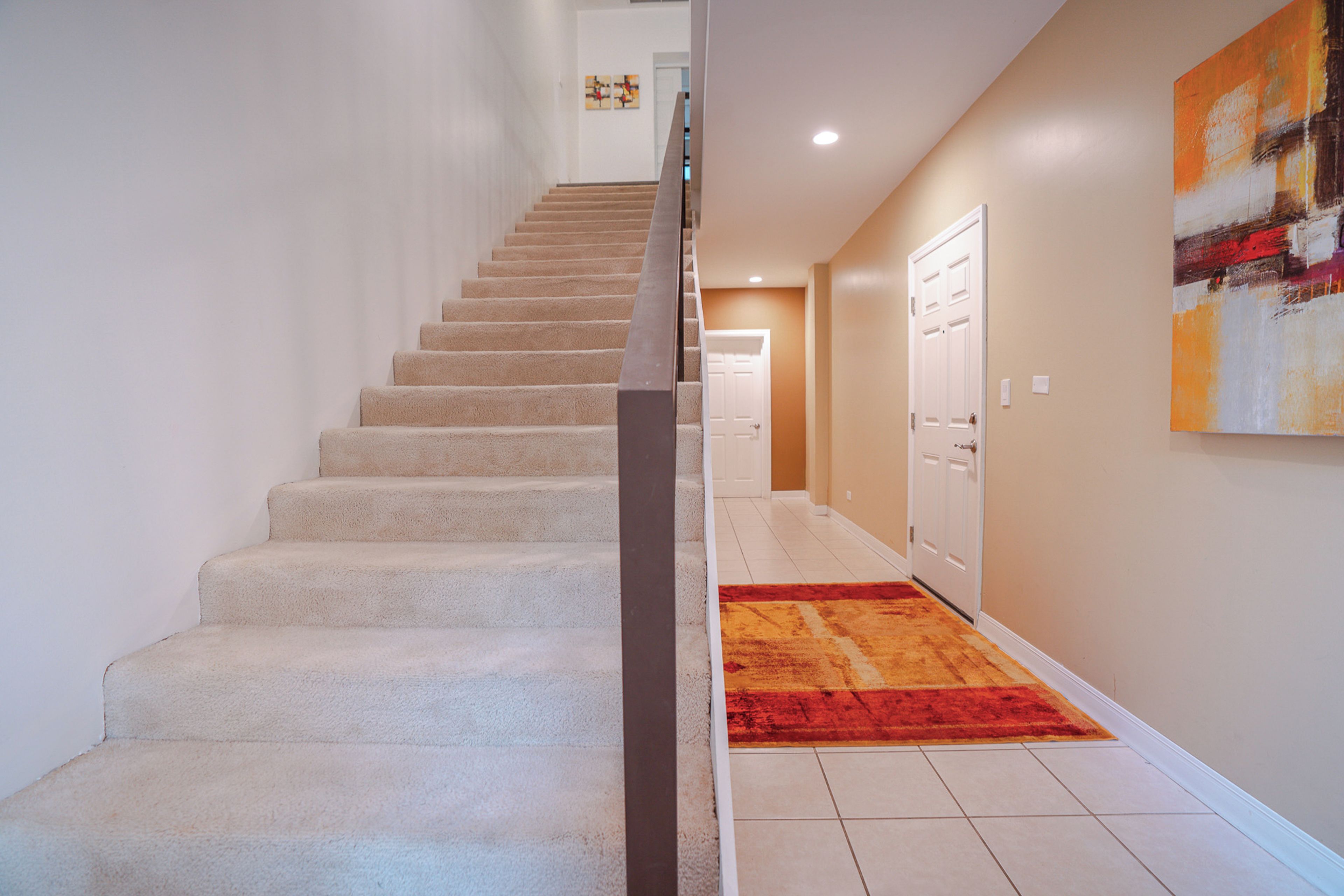 Uma escadaria leva a um patamar com tapete vermelho, paredes brancas e uma porta no final.