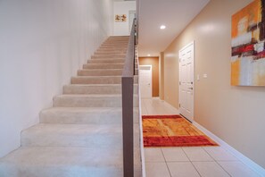 A staircase leading to a landing with a red carpet, white walls, and a door at the end.