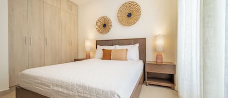 A bedroom with a large bed, wooden wardrobe, two wall-mounted lamps, and a window with curtains.