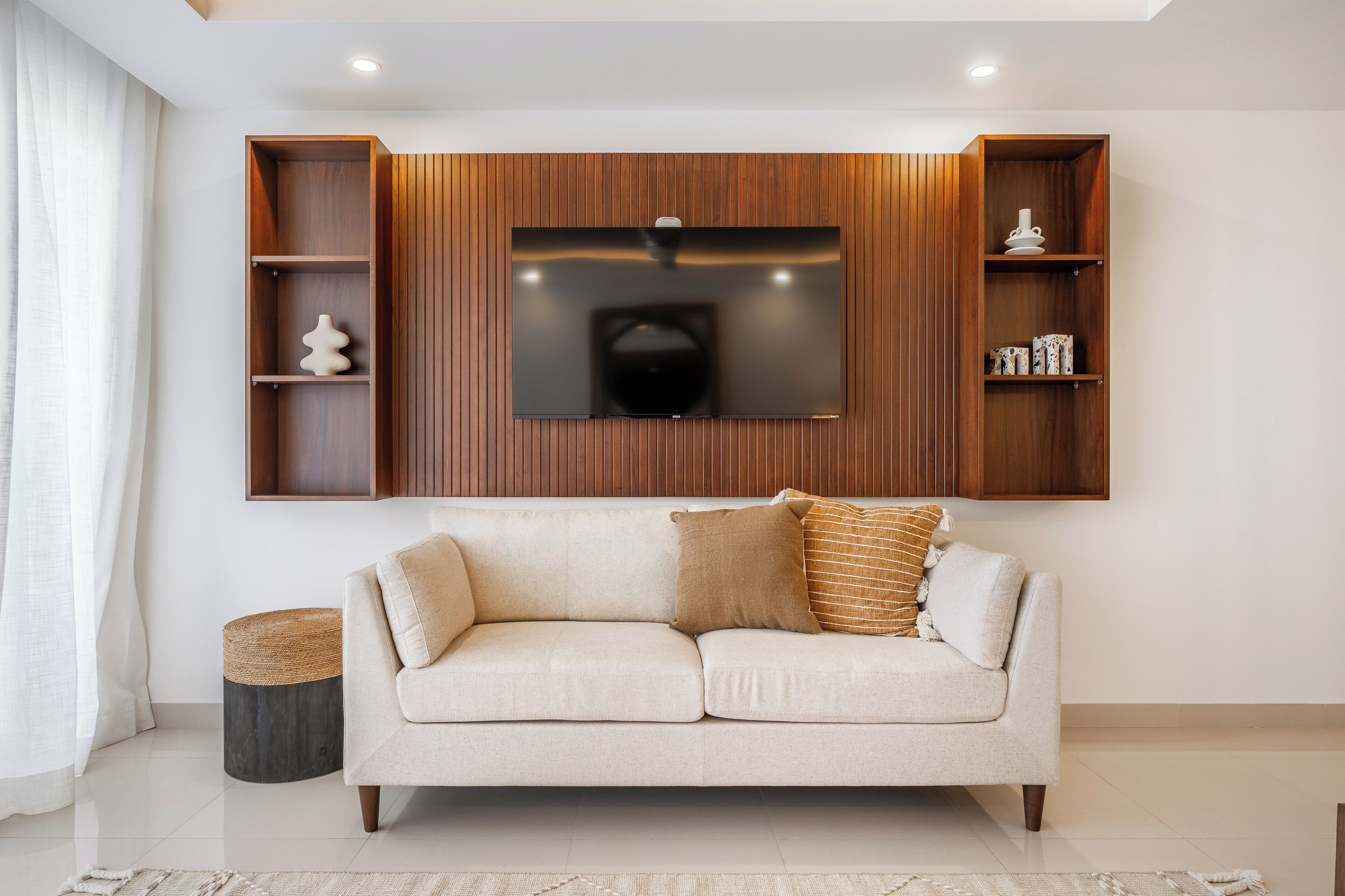 A modern living room with a sofa, a flat-screen TV mounted on a wooden wall, and built-in shelving.