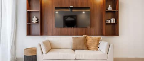 A modern living room with a sofa, a flat-screen TV mounted on a wooden wall, and built-in shelving.