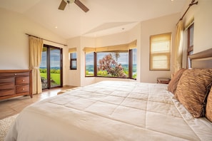 A bedroom with a large bed, a wooden dresser, and a view of the outdoors.