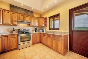 Una cocina con armarios de madera, una estufa de acero inoxidable, un microondas y un ventanal con vistas al campo.
