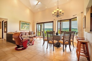 A spacious living room with a large dining table, comfortable seating, and a view of the countryside through large windows.