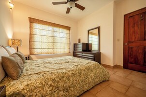 A bedroom with a bed, a dresser, a mirror, a ceiling fan, and a door.