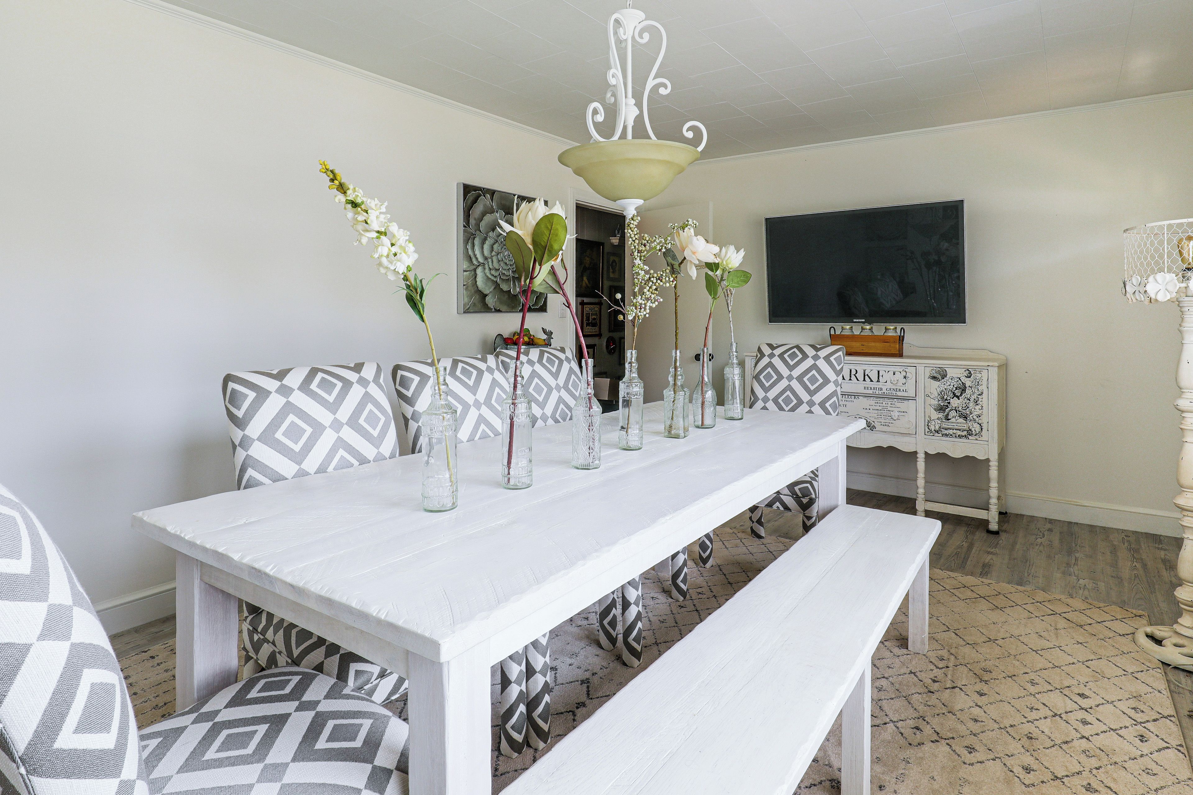Un comedor con una mesa blanca, cojines estampados y un banco.