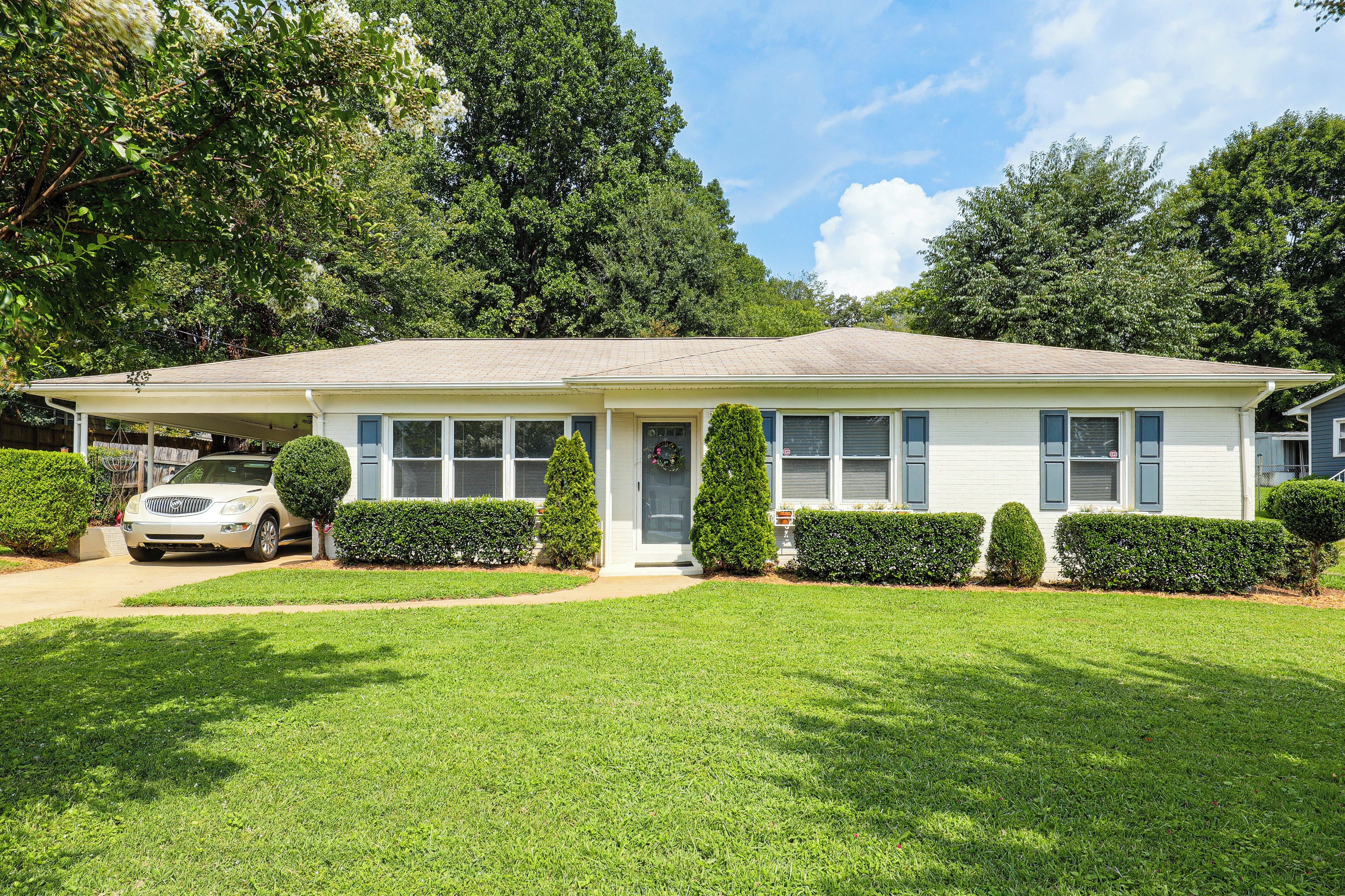 A single-story house with a covered porch, a car parked in front, and well-maintained front yard with hedges.