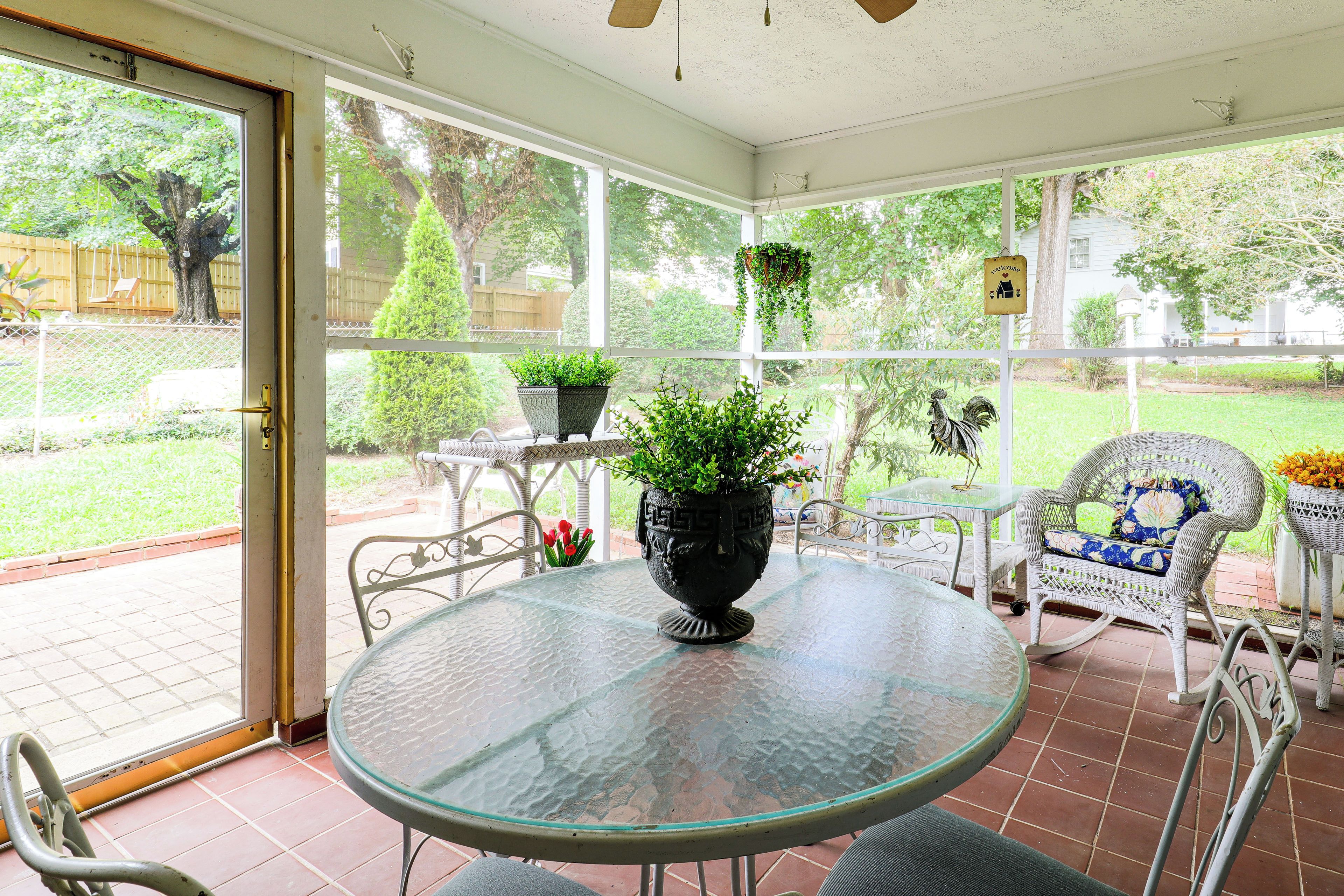 A covered patio with a glass table, chairs, and potted plants.