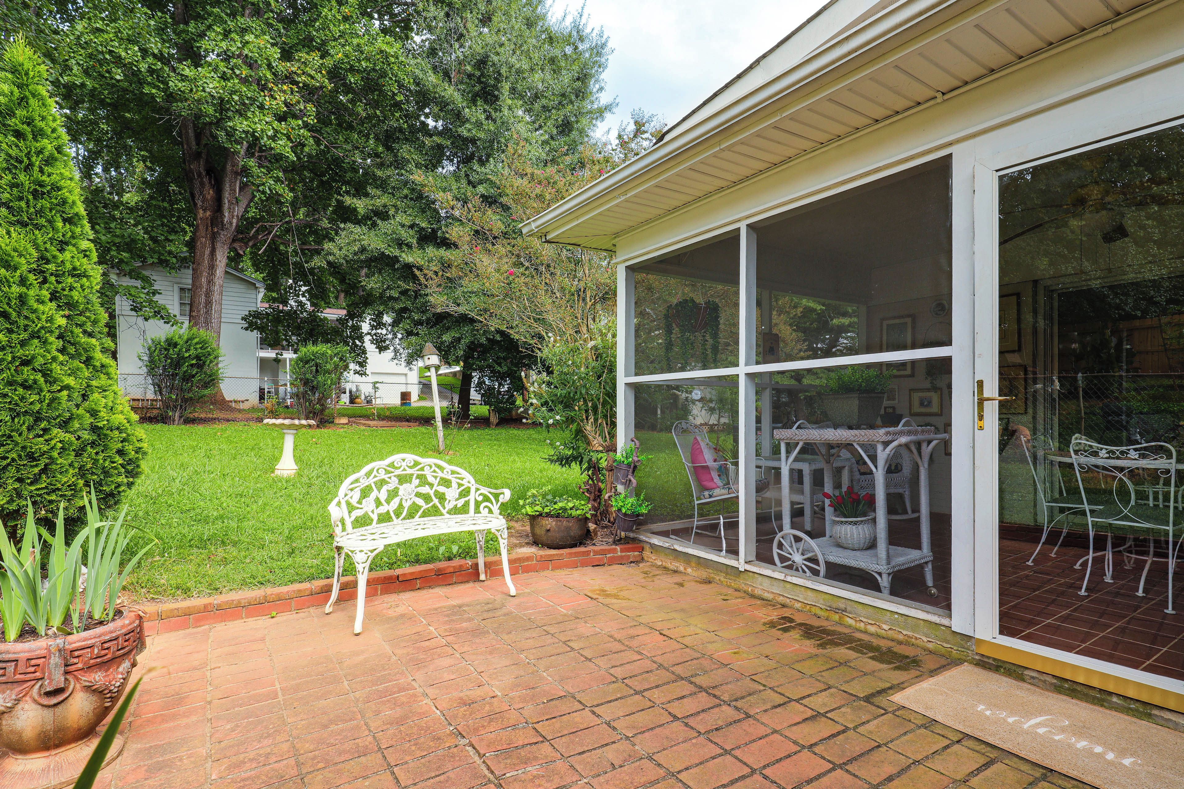 Un patio techado con un banco de metal blanco, una mesa pequeña y una silla.