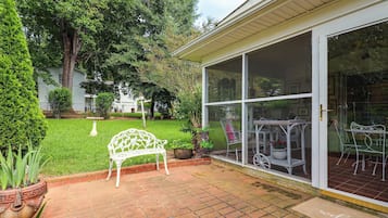 Un patio techado con un banco de metal blanco, una mesa pequeña y una silla.