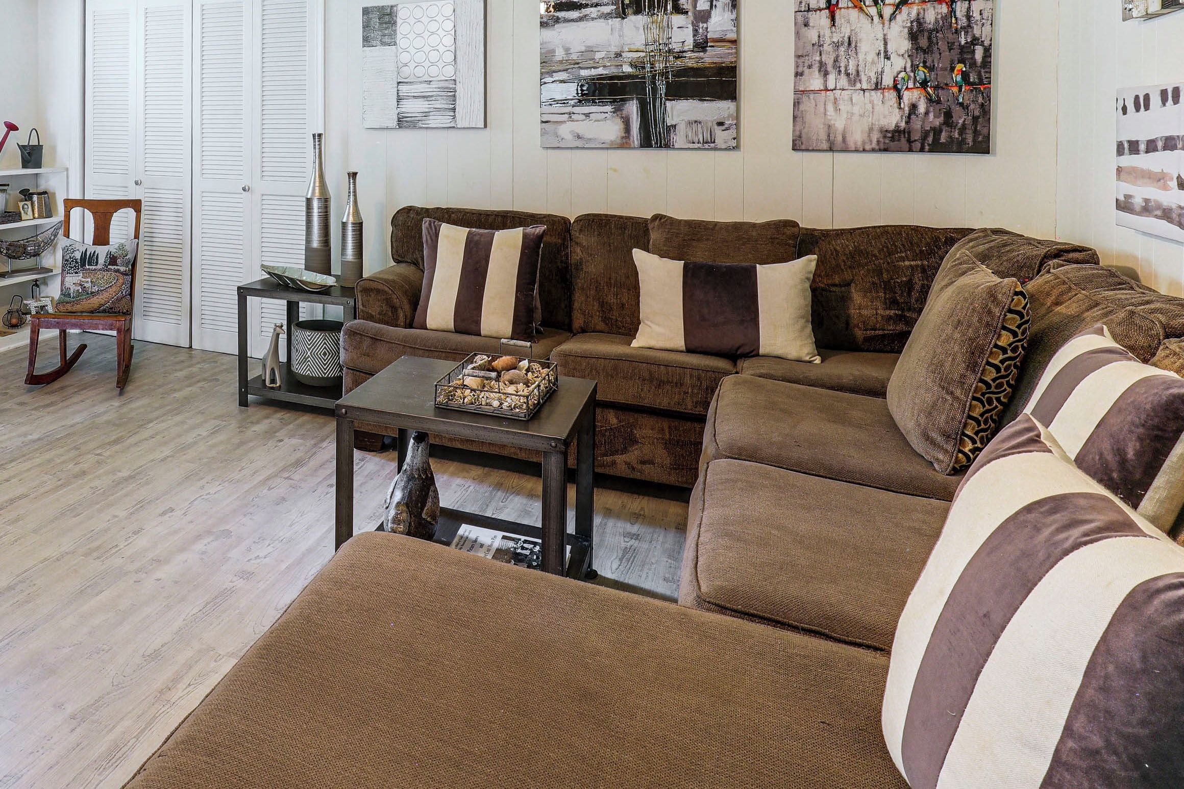A living room with a brown sectional sofa, a coffee table, and a side table with decorative items.