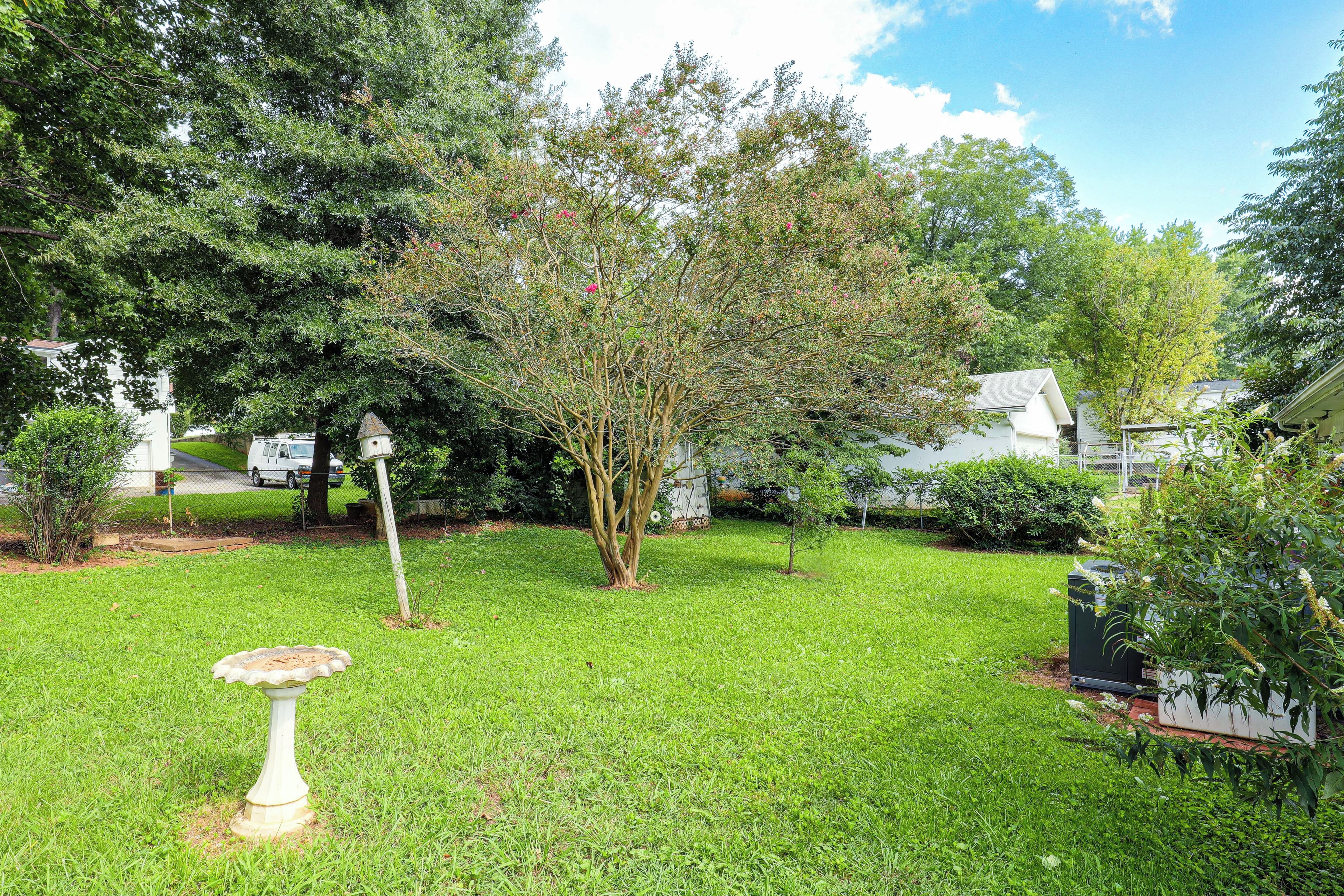 A well-maintained grassy yard with a birdbath, mature trees, and a white building in the background.