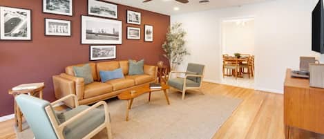 Una sala de estar con un sofá de cuero marrón, dos sillones, una mesa de centro y un comedor con una mesa y sillas.
