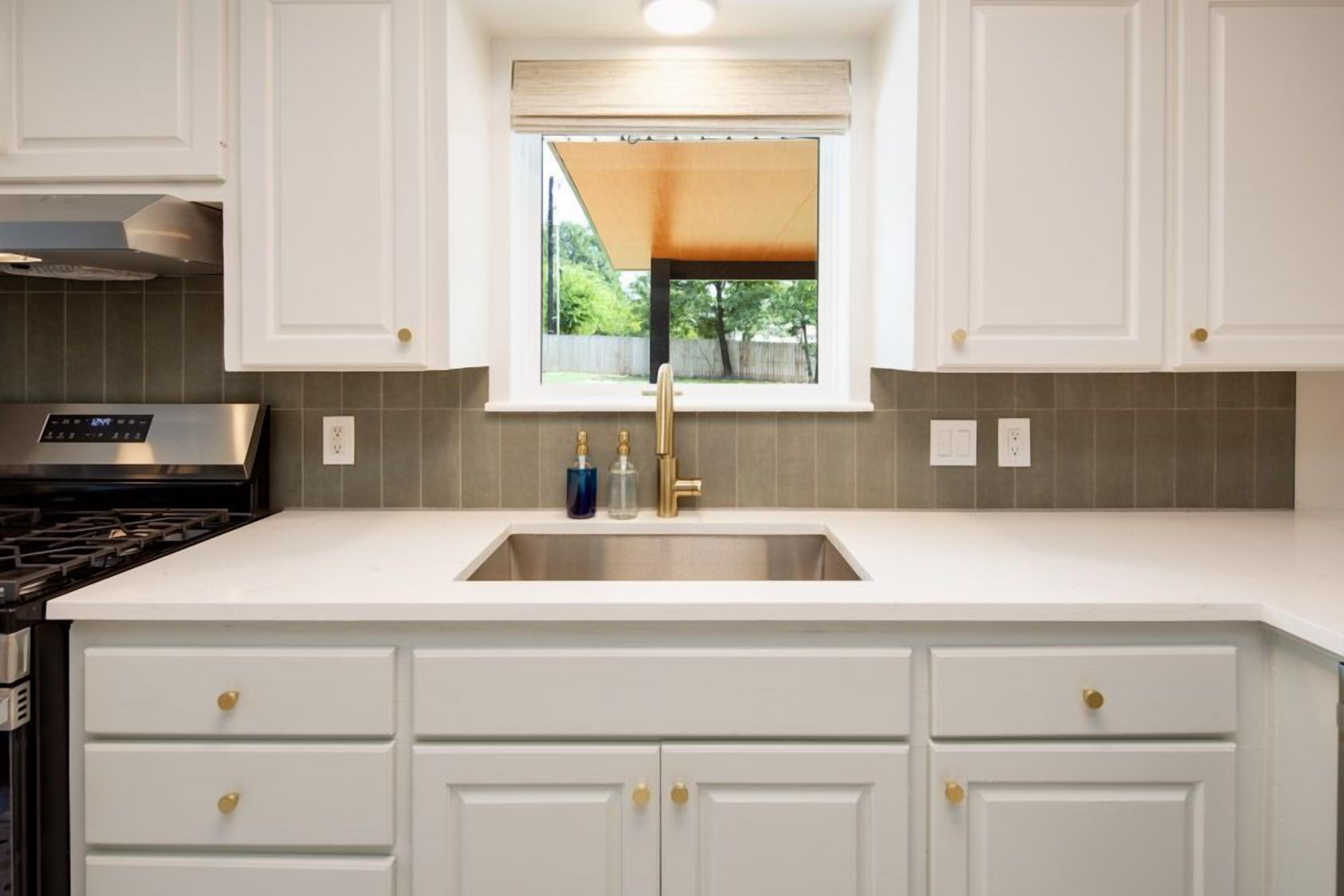 Una cocina con armarios blancos, un lavamanos de acero inoxidable y una ventana con vistas a la vegetación.
