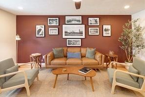 A living room with a brown leather sofa, two armchairs, a coffee table, and a wall adorned with framed black and white photographs.