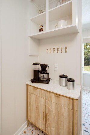 A kitchen with a coffee station, including a coffee maker, two thermoses, and a shelf with kitchenware.